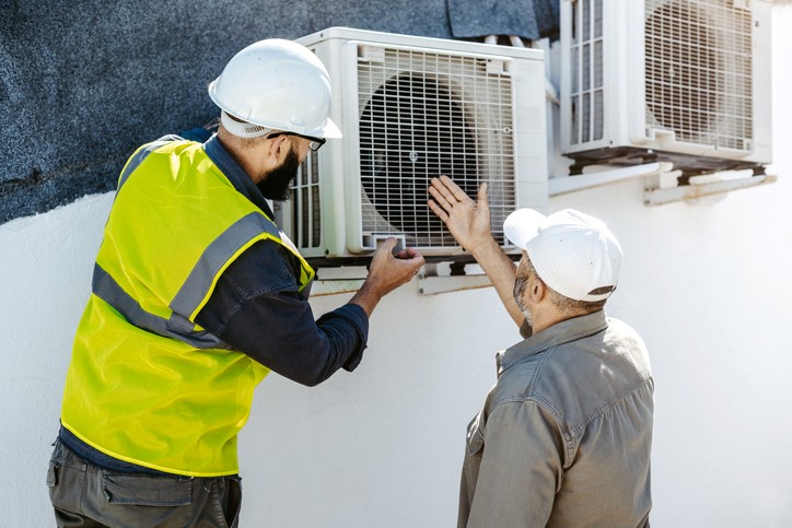 HVAC technician inspecting outdoor air conditioning unit with homeowner