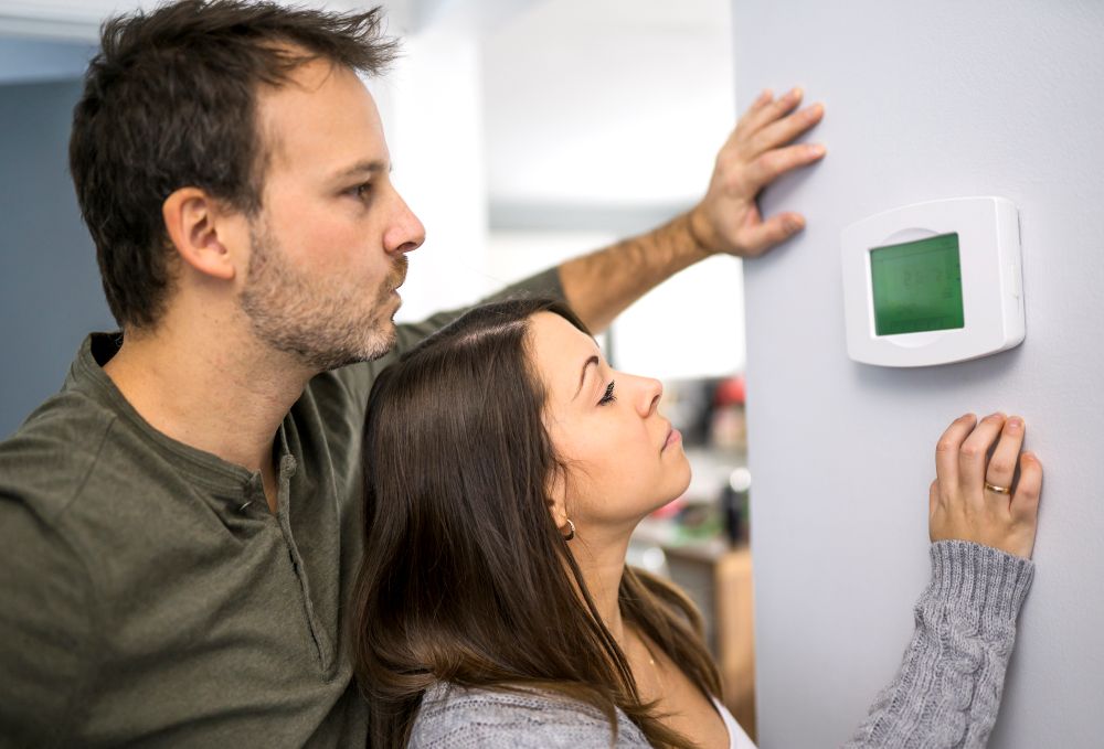 Homeowners adjusting thermostat while troubleshooting furnace heating issues